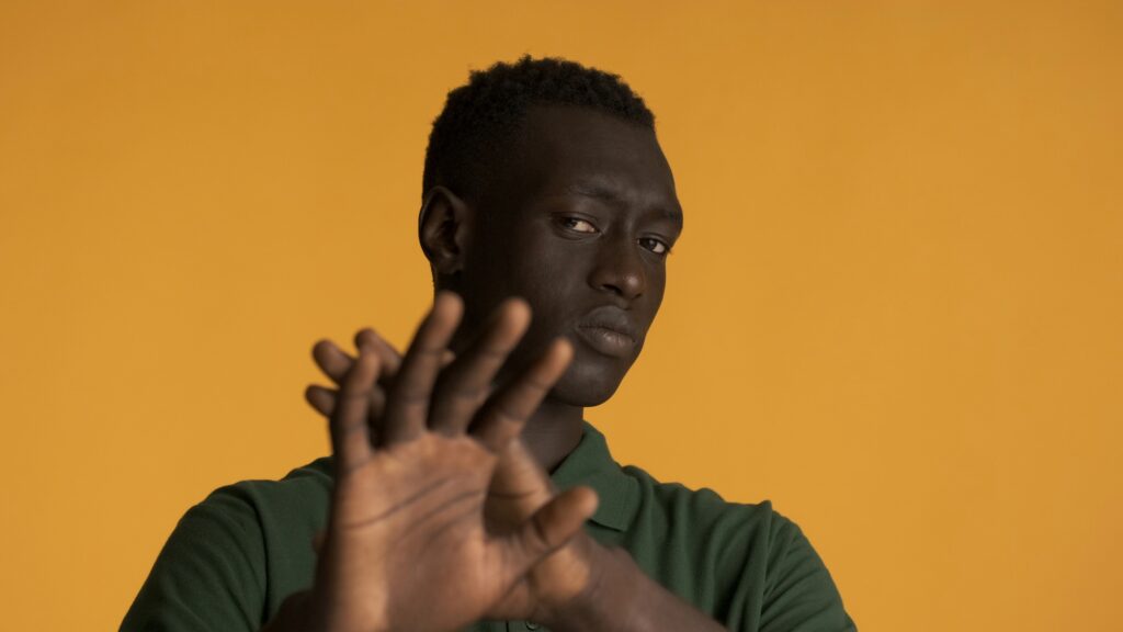 African American man looking serious showing stop gesture over yellow background. Don't want