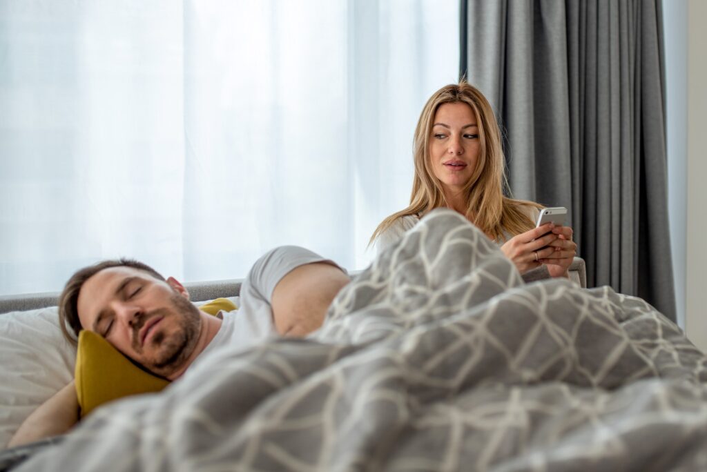 Caucasian couple with suspicious wife checking husband's phone while he is sleeping