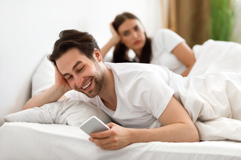 Cheating Husband Texting On Phone Ignoring Wife Lying In Bed