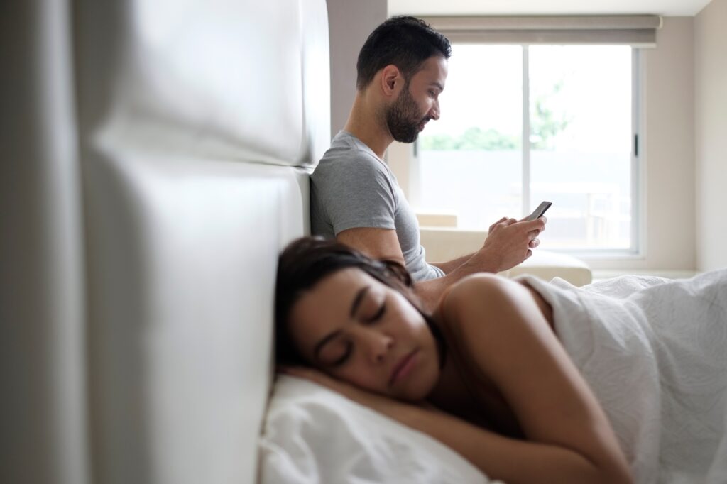 Couple In Bed With Cheating Man Texting On Smartphone