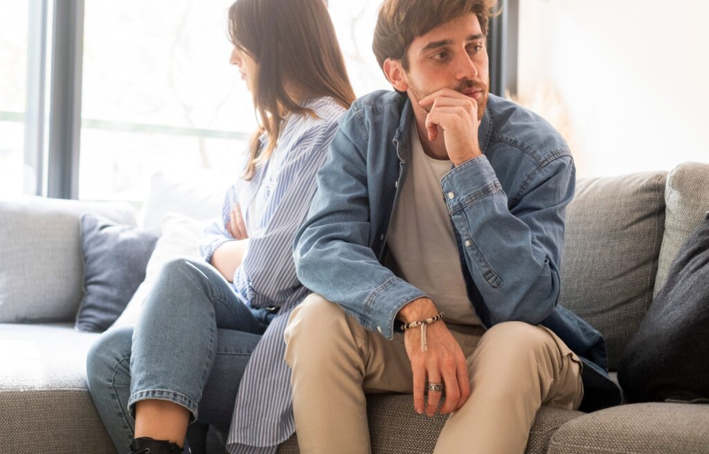 Engaged couple with relationship problems sitting on the sofa with their backs