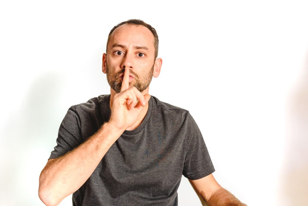 Man in studio asking for silence with a wave of his hand putting a finger on his lips