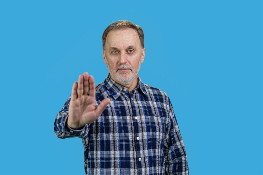 Portrait of mature senior man showing his palm as stop gesture sign.