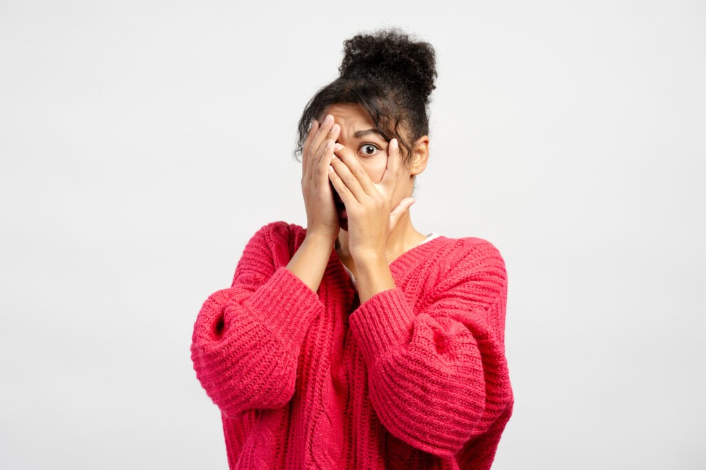 Scared young woman covering face with hands showing fear