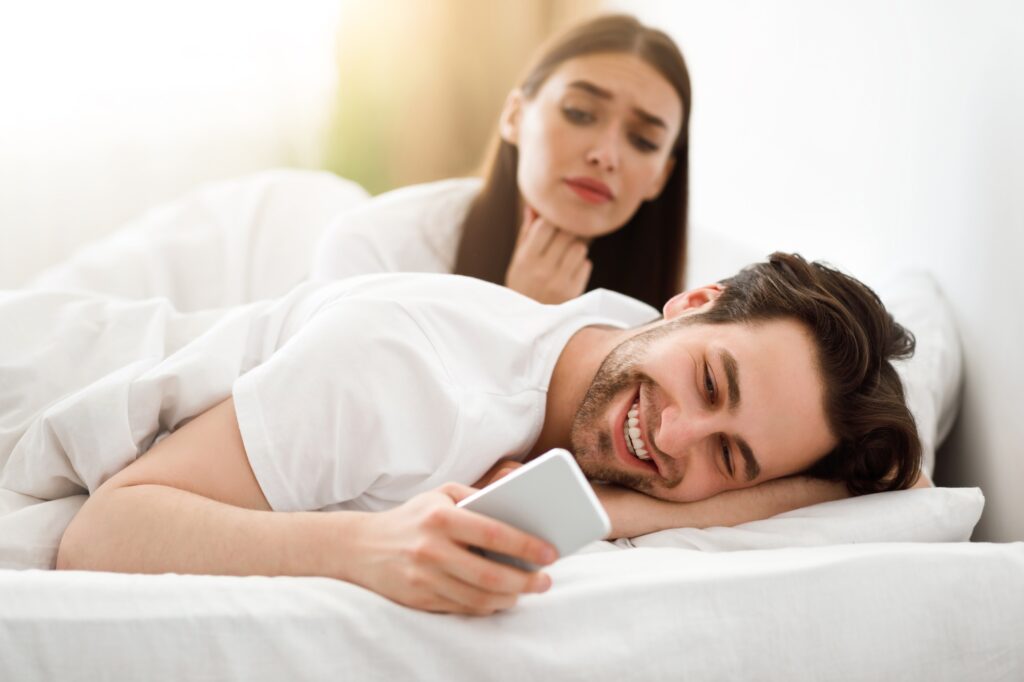 Wife Spying While Cheating Husband Texting On Cellphone In Bedroom