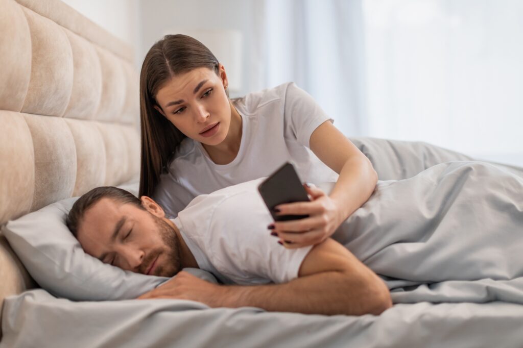 Anxious woman checking phone beside sleeping man