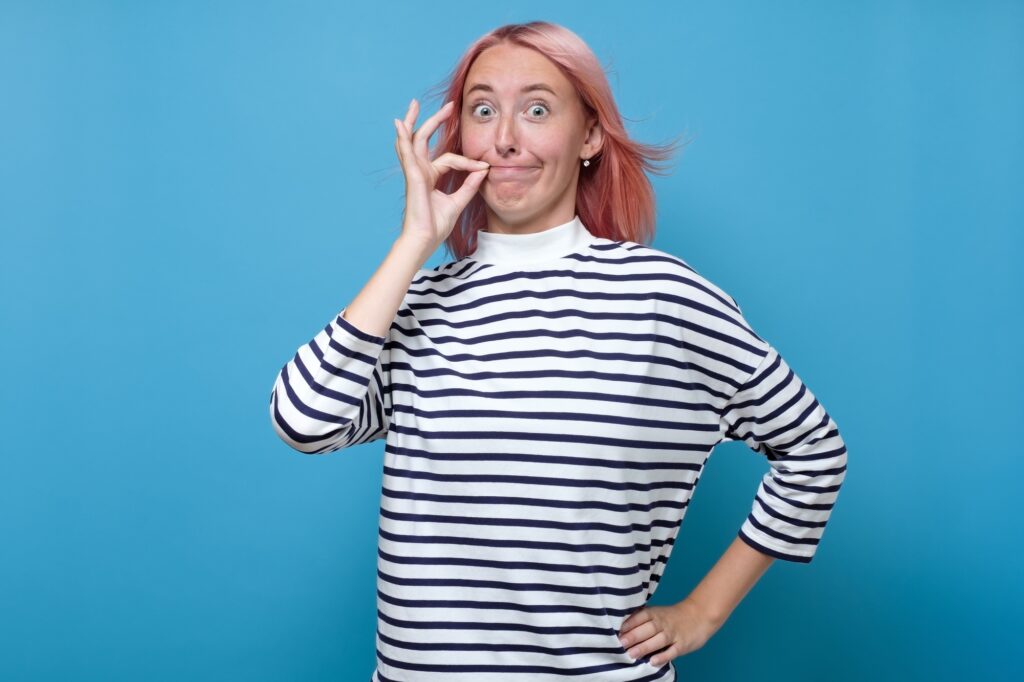 Caucasian woman with pink hair zipping her mouth shut